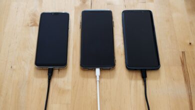 Three smartphones connected to chargers on a wooden surface, showcasing modern technology