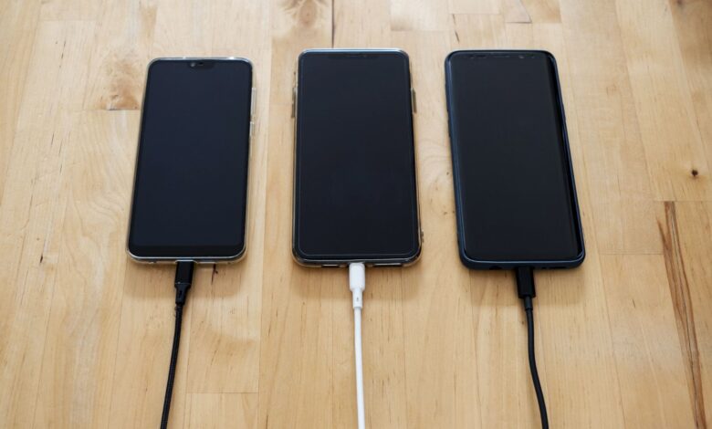 Three smartphones connected to chargers on a wooden surface, showcasing modern technology