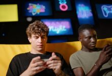 Two friends play mobile games indoors, focusing intently on their smartphones.