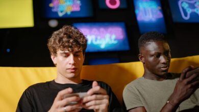 Two friends play mobile games indoors, focusing intently on their smartphones.