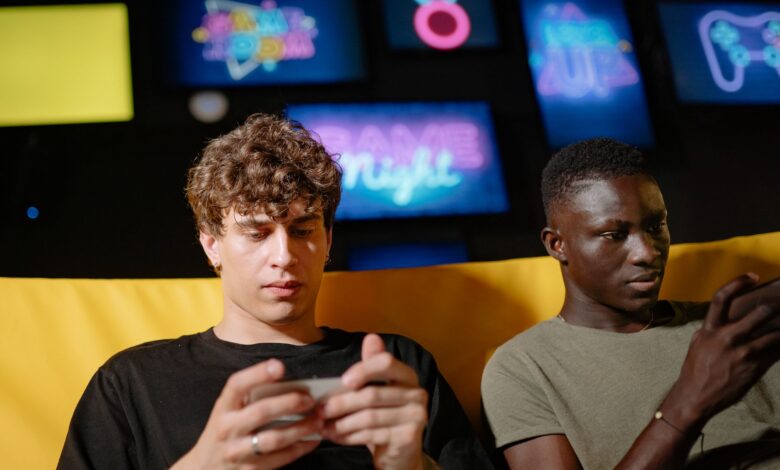 Two friends play mobile games indoors, focusing intently on their smartphones.