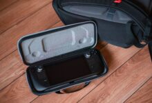 A portable gaming console in a protective case on wooden floor with backpack.