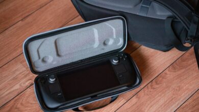 A portable gaming console in a protective case on wooden floor with backpack.