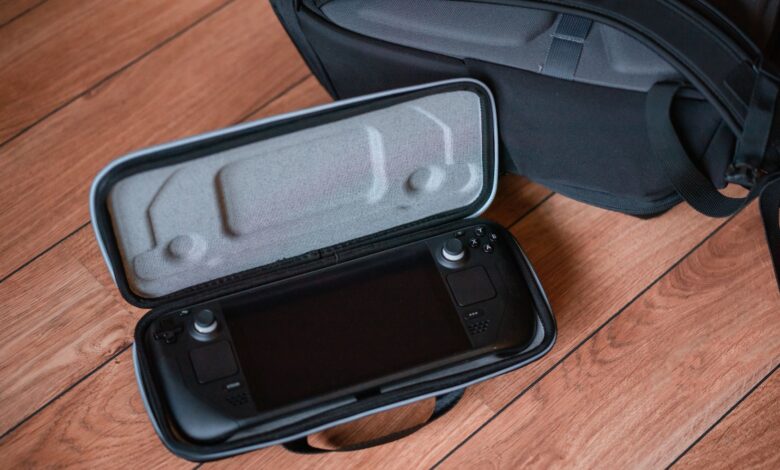 A portable gaming console in a protective case on wooden floor with backpack.