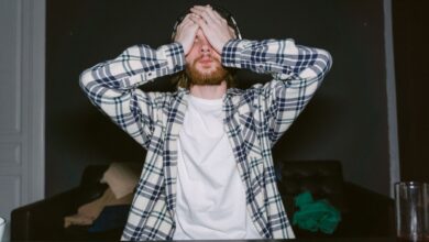Focused male gamer in plaid shirt, showing stress with hands on face, indoors.