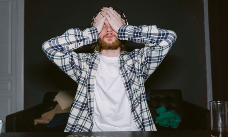 Focused male gamer in plaid shirt, showing stress with hands on face, indoors.