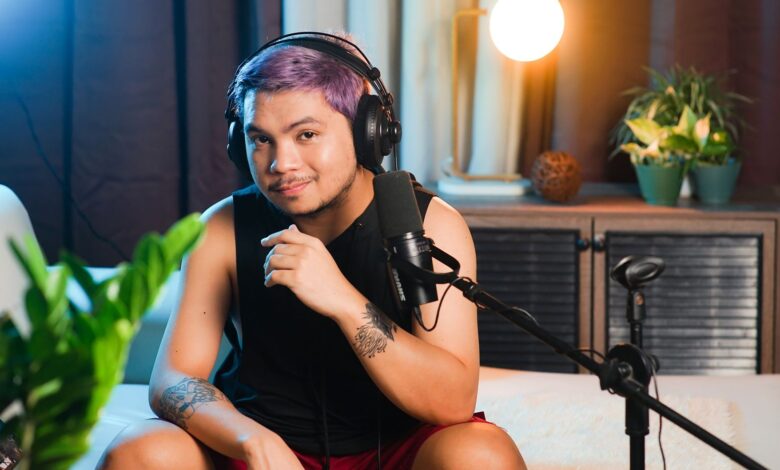 Musician sitting indoors with headphones and microphone, ready to record a podcast.