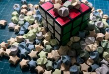 A Rubik's cube surrounded by pastel origami stars on a blue gridded surface.