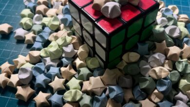 A Rubik's cube surrounded by pastel origami stars on a blue gridded surface.