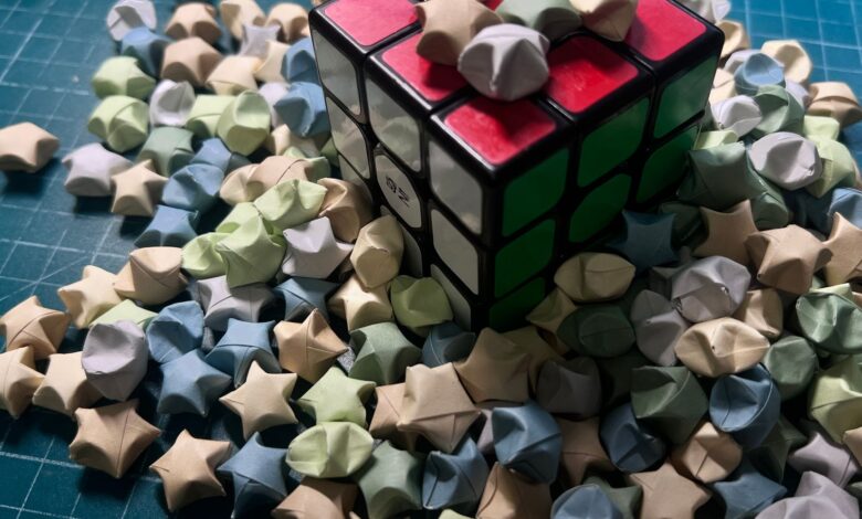 A Rubik's cube surrounded by pastel origami stars on a blue gridded surface.