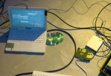 An overhead view of a vintage electronics setup featuring a laptop and disks with tangled cables.