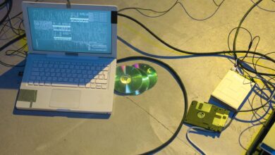 An overhead view of a vintage electronics setup featuring a laptop and disks with tangled cables.