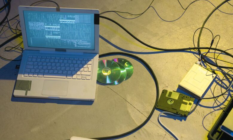 An overhead view of a vintage electronics setup featuring a laptop and disks with tangled cables.