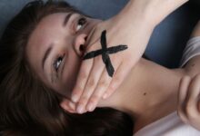 A conceptual portrait of a woman with a marked hand over her mouth, symbolizing silence or censorship.