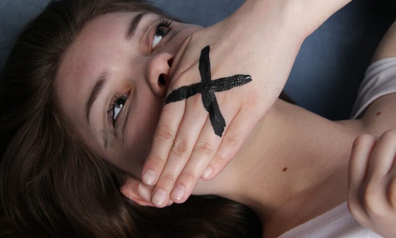 A conceptual portrait of a woman with a marked hand over her mouth, symbolizing silence or censorship.