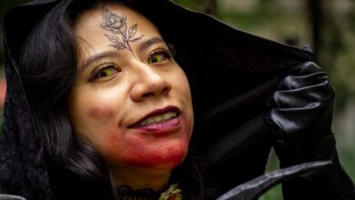 Close-up of a woman in vampire cosplay, featuring a rose tattoo and yellow contact lenses, outdoors.