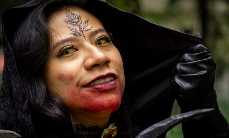 Close-up of a woman in vampire cosplay, featuring a rose tattoo and yellow contact lenses, outdoors.