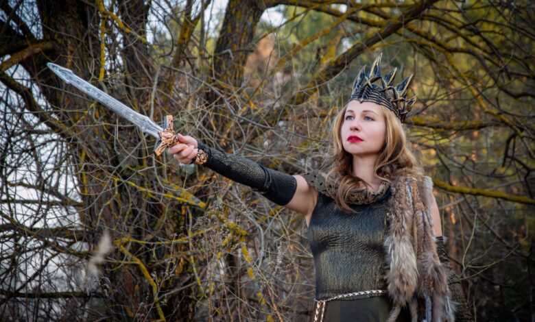 A fierce warrior queen in medieval costume holding a sword against a forest backdrop.