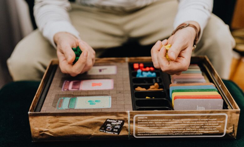 Person playing a board game with colorful pieces and cards indoors, focused and engaging.