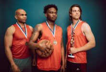 Three basketball players celebrating with medals and a trophy in victory pose.