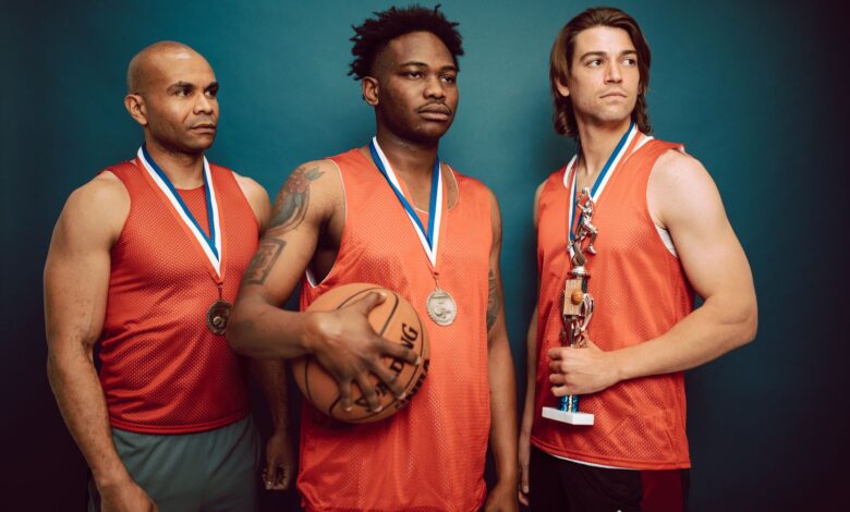 Three basketball players celebrating with medals and a trophy in victory pose.