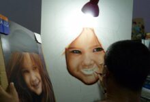 Artist paints a realistic portrait of a smiling child under a lamp.