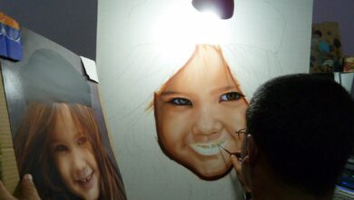 Artist paints a realistic portrait of a smiling child under a lamp.