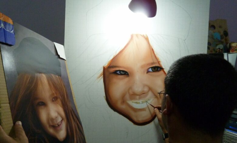 Artist paints a realistic portrait of a smiling child under a lamp.
