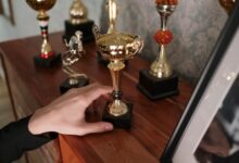 A close-up of a hand reaching for a shiny trophy on a wooden shelf, symbolizing success.