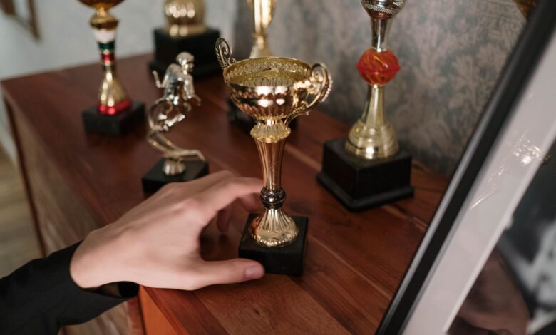 A close-up of a hand reaching for a shiny trophy on a wooden shelf, symbolizing success.