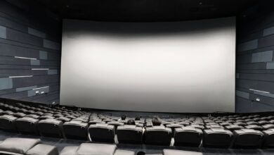 Spacious empty movie theater with a few people seated and a large blank screen.