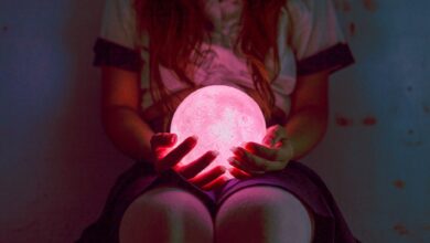 A captivating image of a woman holding a glowing pink sphere in dim lighting, evoking mystery and magic.