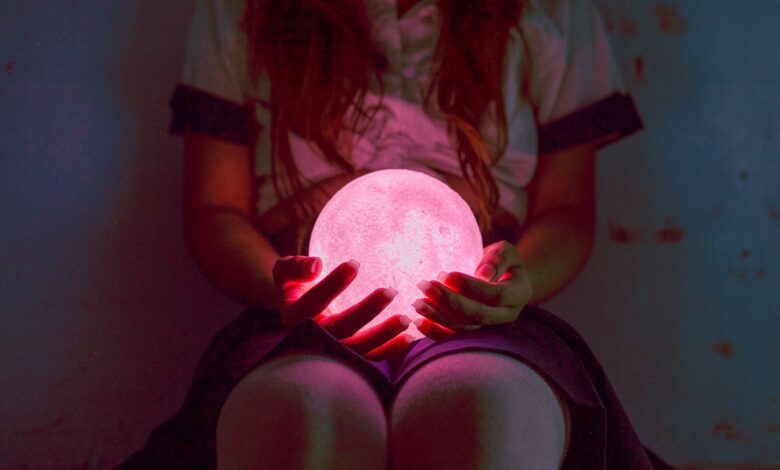 A captivating image of a woman holding a glowing pink sphere in dim lighting, evoking mystery and magic.