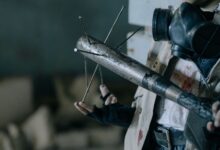 Close-up of a person with a gas mask holding a makeshift melee weapon in a post-apocalyptic setting.