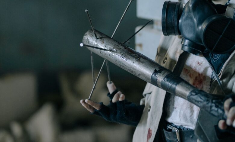 Close-up of a person with a gas mask holding a makeshift melee weapon in a post-apocalyptic setting.