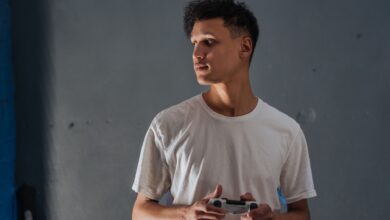 A young man wearing a white t-shirt focuses intently while holding a game controller indoors.