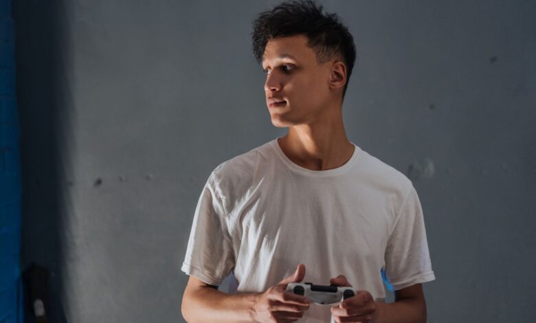 A young man wearing a white t-shirt focuses intently while holding a game controller indoors.