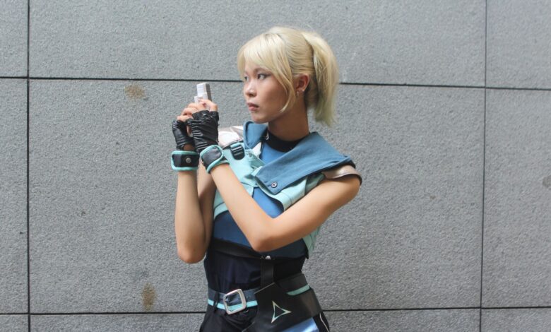 Young woman in futuristic cosplay outfit holding a blaster, posing against a neutral background.