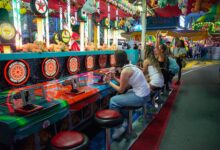 Friends enjoying a lively carnival game at night with colorful lights and plush toys all around.