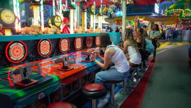 Friends enjoying a lively carnival game at night with colorful lights and plush toys all around.