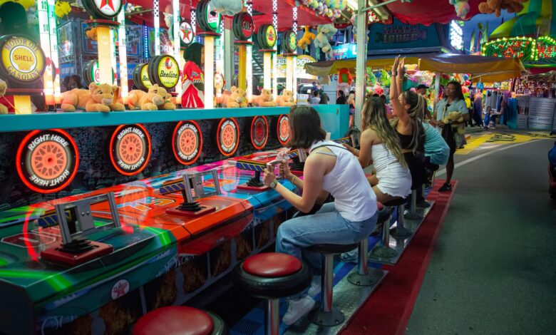 Friends enjoying a lively carnival game at night with colorful lights and plush toys all around.