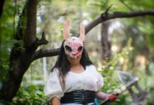 Cosplayer in a forest wearing a distinctive mask, conveying a mysterious theme.