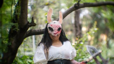 Cosplayer in a forest wearing a distinctive mask, conveying a mysterious theme.