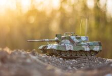 A detailed model tank positioned on gravel terrain with a warm, golden hour glow in the background.