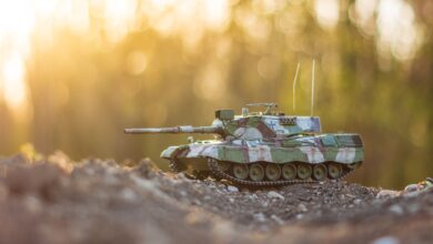 A detailed model tank positioned on gravel terrain with a warm, golden hour glow in the background.