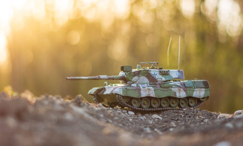 A detailed model tank positioned on gravel terrain with a warm, golden hour glow in the background.