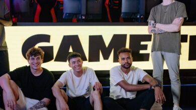 Four young men posing confidently in an eSports arena with gaming setups in the background.