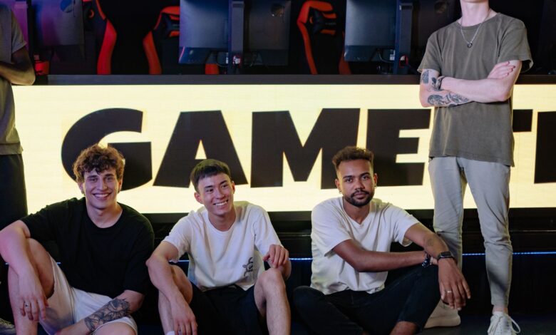 Four young men posing confidently in an eSports arena with gaming setups in the background.