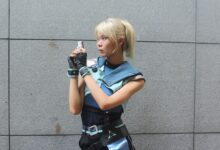 Young woman in futuristic cosplay outfit holding a blaster, posing against a neutral background.