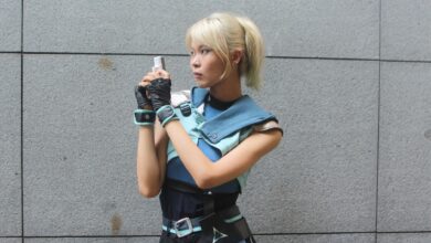 Young woman in futuristic cosplay outfit holding a blaster, posing against a neutral background.